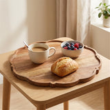 A scalloped wooden serving tray displayed on a light wood table, styled with a cup of coffee, a small bowl of mixed berries, and a croissant in a bright, modern room.