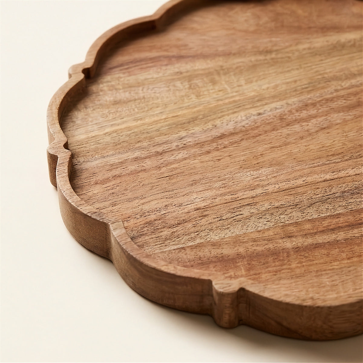 A close-up of a scalloped wooden serving tray with a warm medium-brown wood grain finish, set against a clean off-white background.