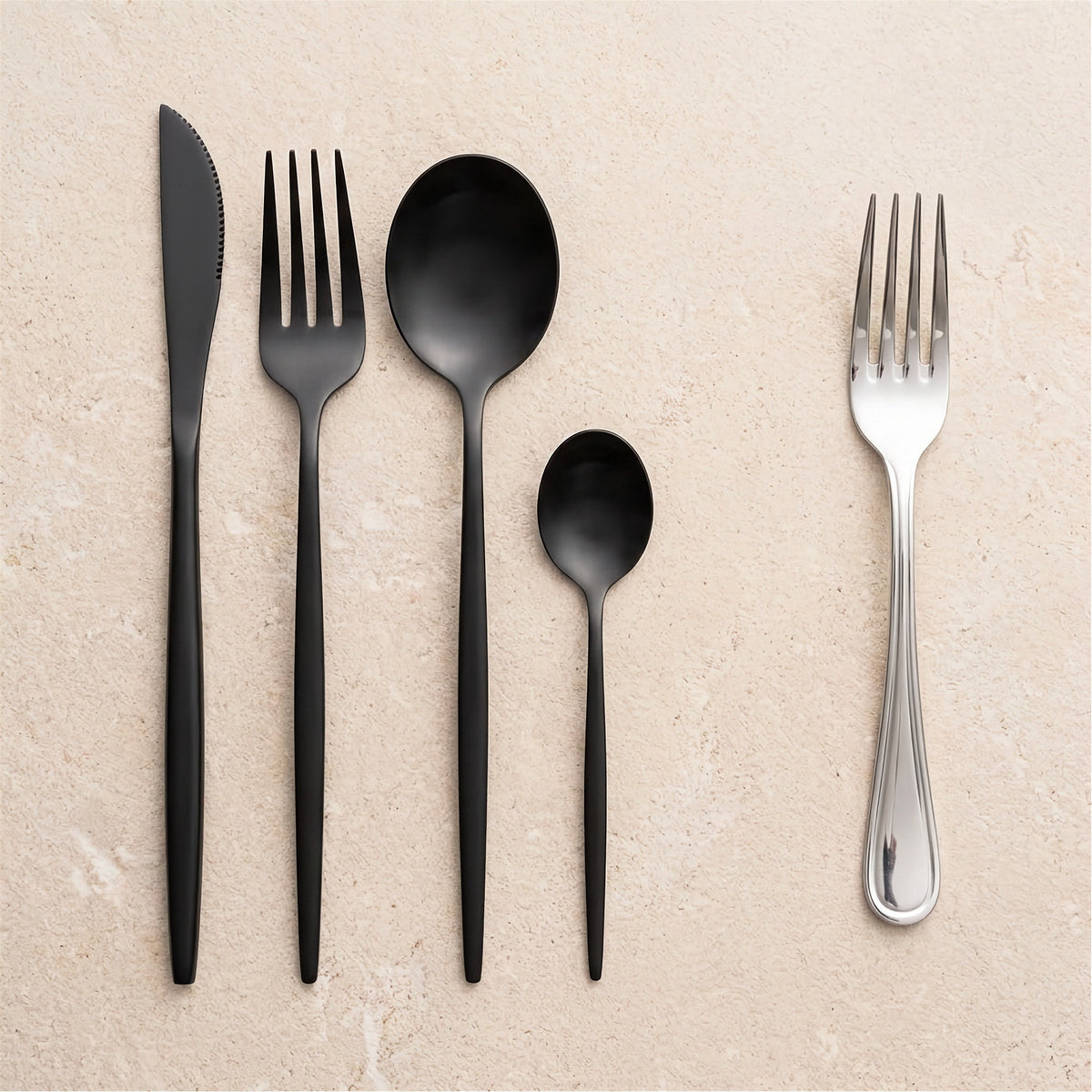 Five-piece flatware set arranged on a light beige stone surface, including a black knife, black plastic fork, black spoon, small black spoon, and a silver metal fork.