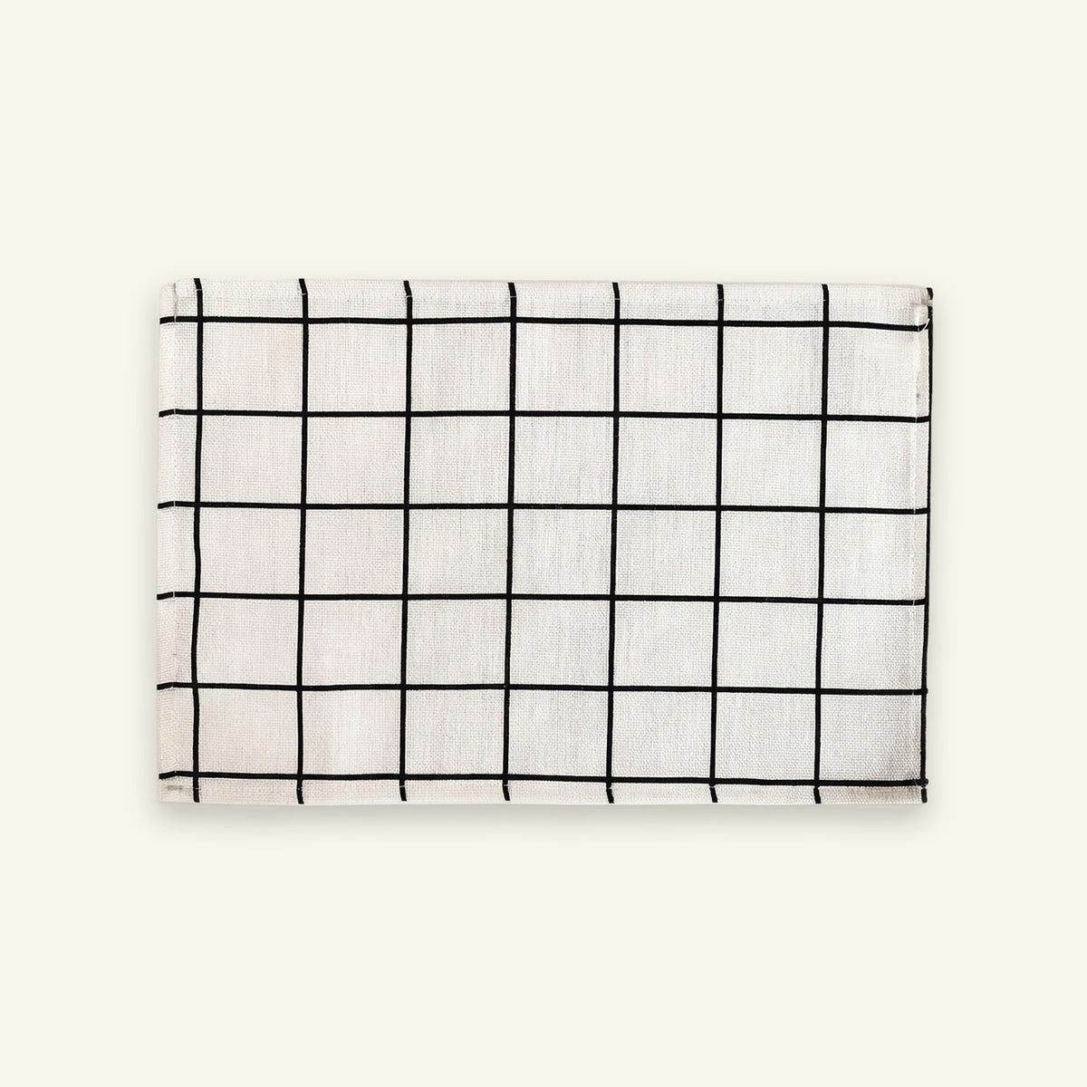 A rectangular white fabric item, likely a napkin or small towel, featuring a black grid pattern, displayed flat against a solid off-white background.