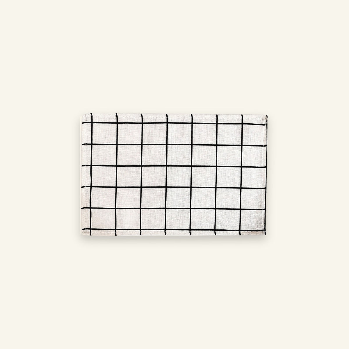 A rectangular white fabric item, likely a napkin or small towel, featuring a black grid pattern, displayed against a solid off-white background.