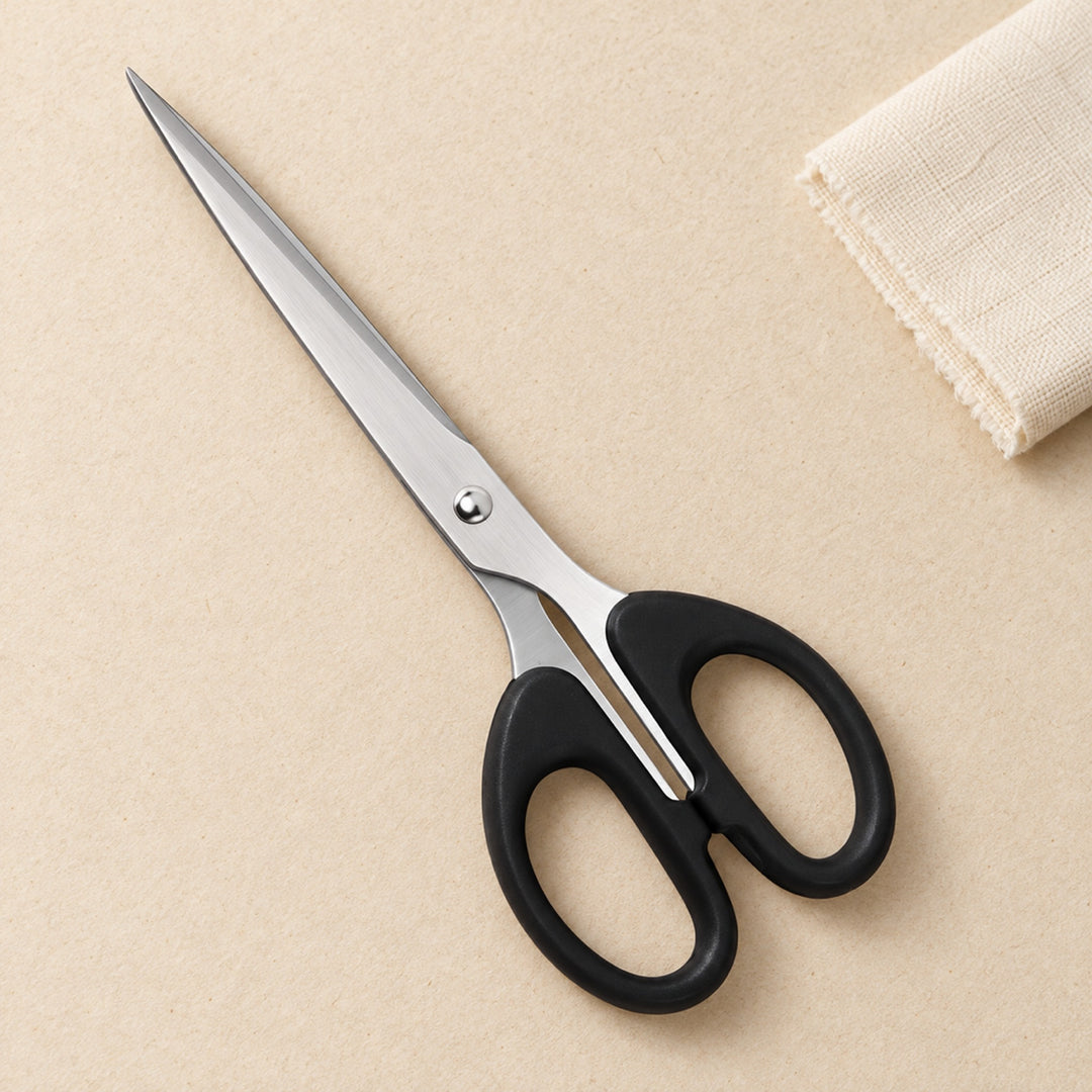 Stainless steel household scissors with black oval soft-grip handles on a warm ivory surface