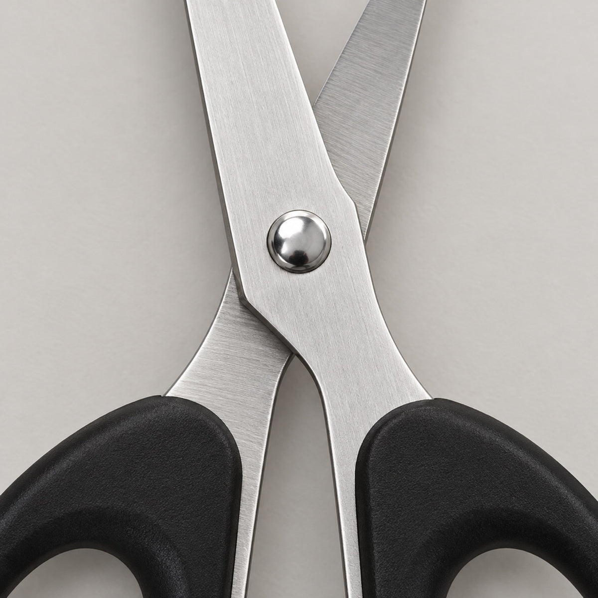 Close-up of the brushed stainless steel blades and metal pivot screw of the black-handled scissors