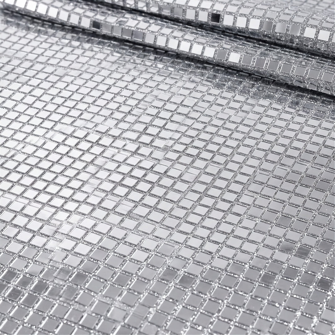 A close-up of a silver mirrored mesh fabric with small square reflective tiles, shown folded to reveal its texture and reflective properties.