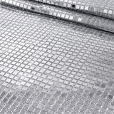 A close-up of a silver mirrored mesh fabric with small square reflective tiles, shown folded to reveal its texture and reflective properties.