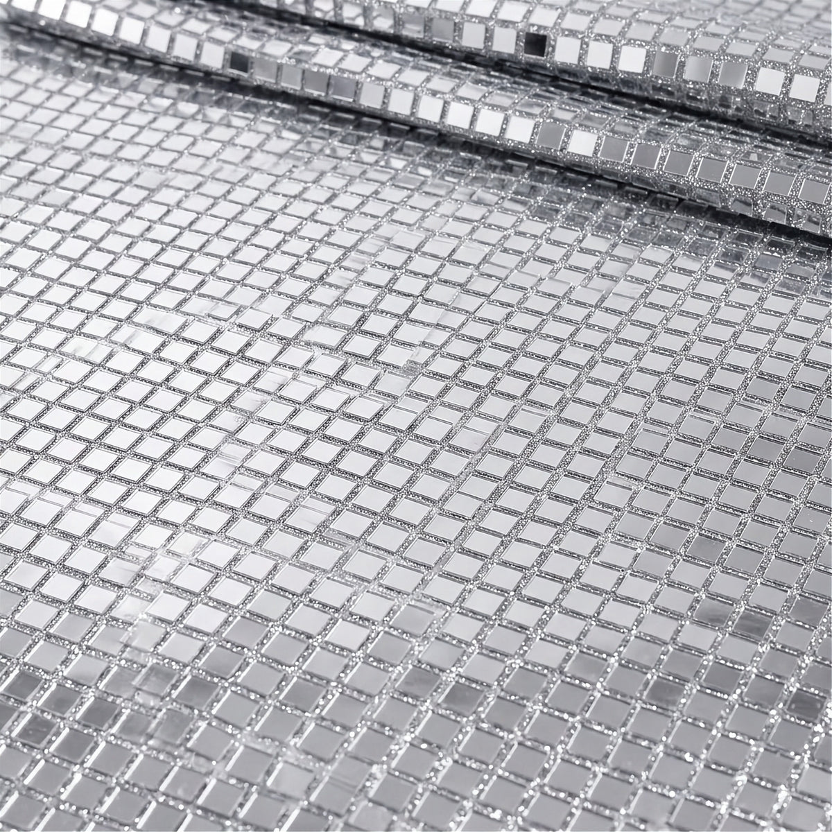 A close-up of a silver mirrored mesh fabric with small square reflective tiles, shown folded to reveal its texture and reflective properties.
