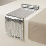 A roll of silver mirrored table runners is partially unrolled on a white table next to a beige fabric runner.