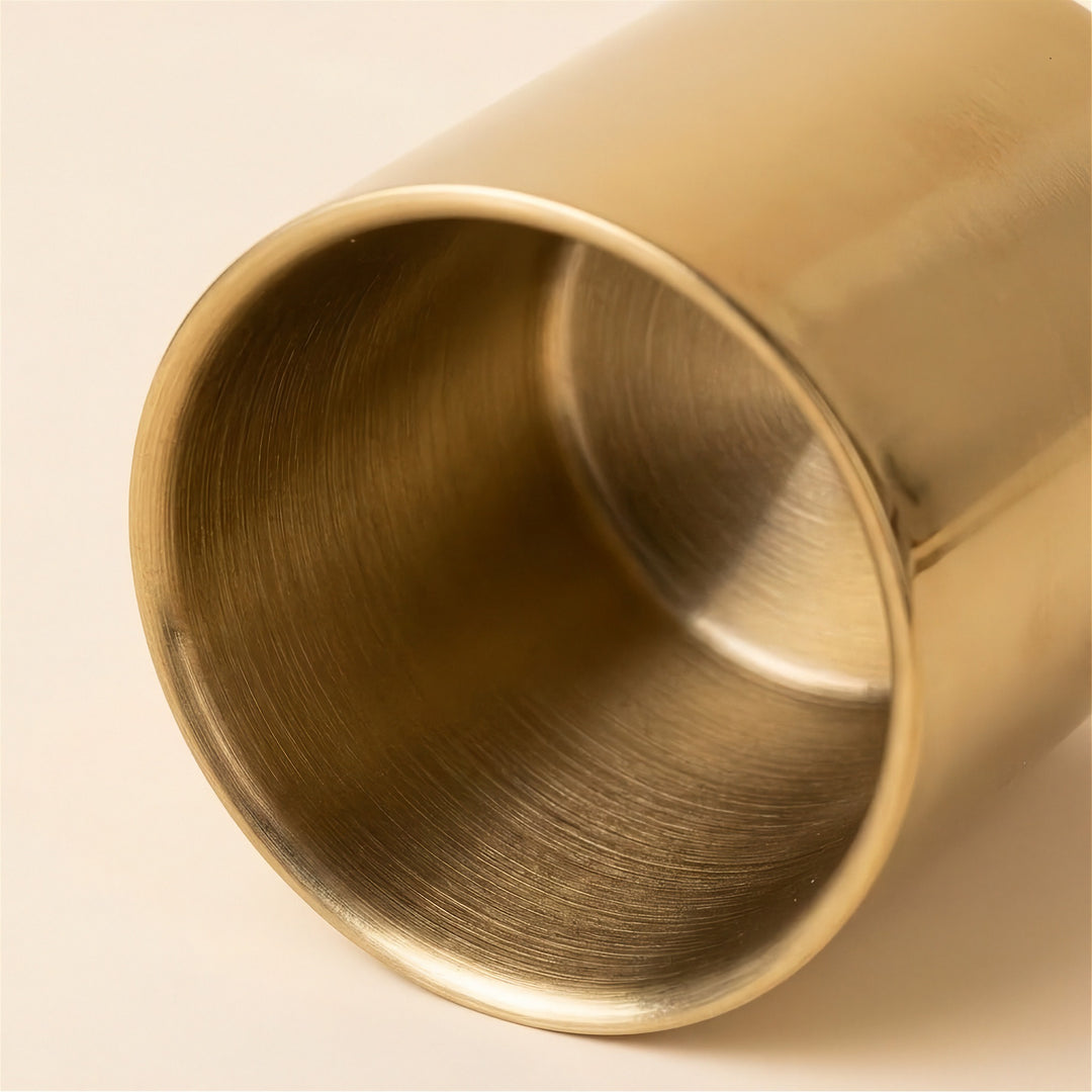 Close-up of a brushed brass cylindrical cup or vase showing the polished metallic interior and rim on a light beige background.