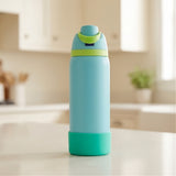 A light blue water bottle with a bright green lid and teal base, standing on a white kitchen counter with a blurred kitchen background.