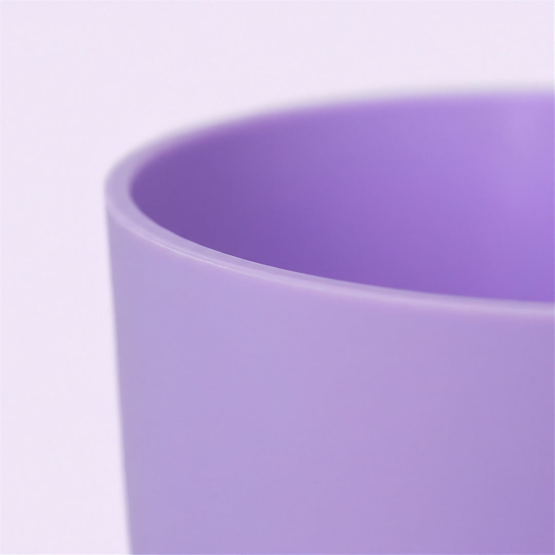 A close-up of a matte lavender purple cylindrical cup or tumbler against a very light lavender background.