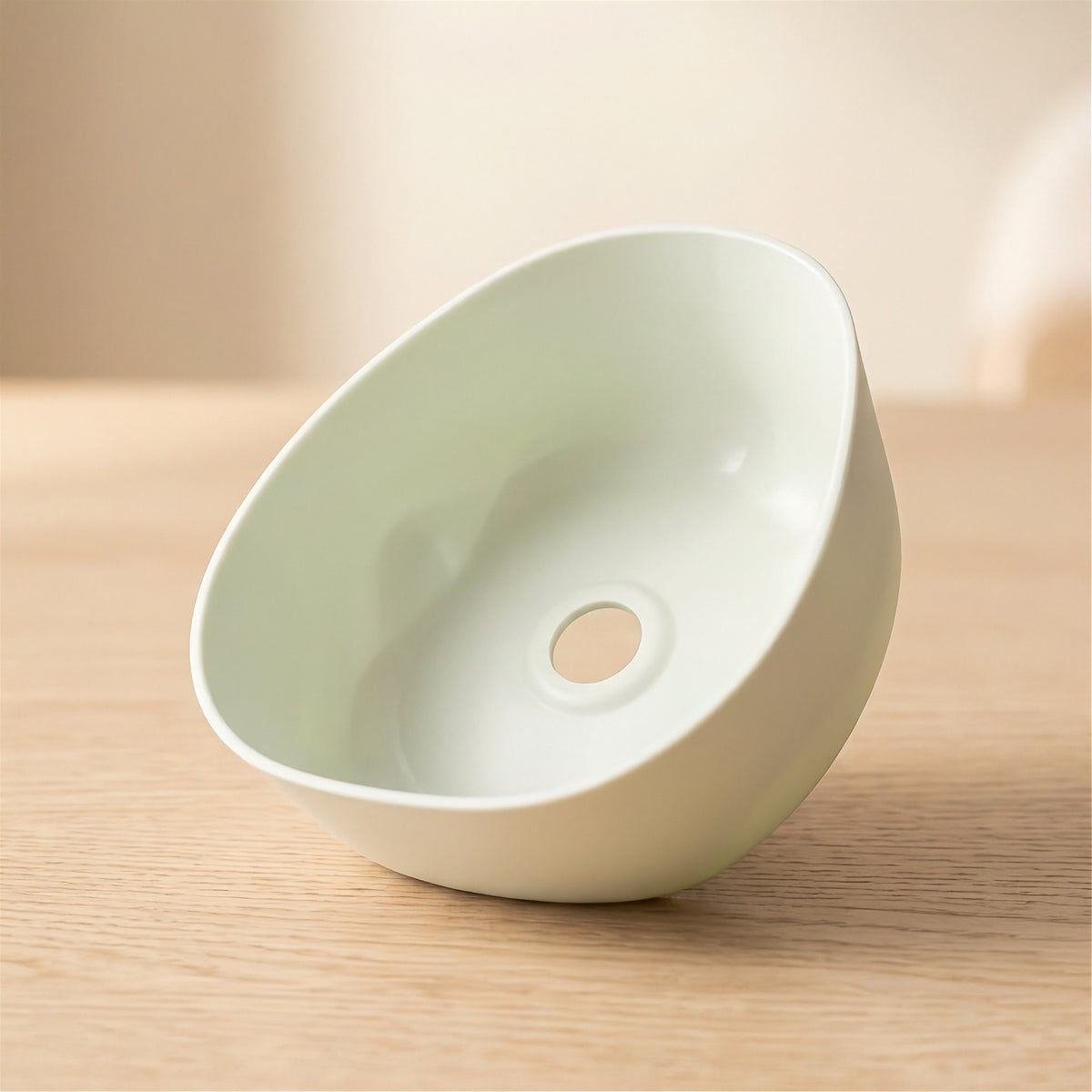 A small off-white ceramic bowl with a circular hole in the center, shown on a light wood surface against a soft beige background.
