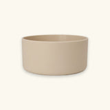 A minimalist, matte ceramic bowl in a light beige color, shown from a front-facing perspective against a solid cream background.