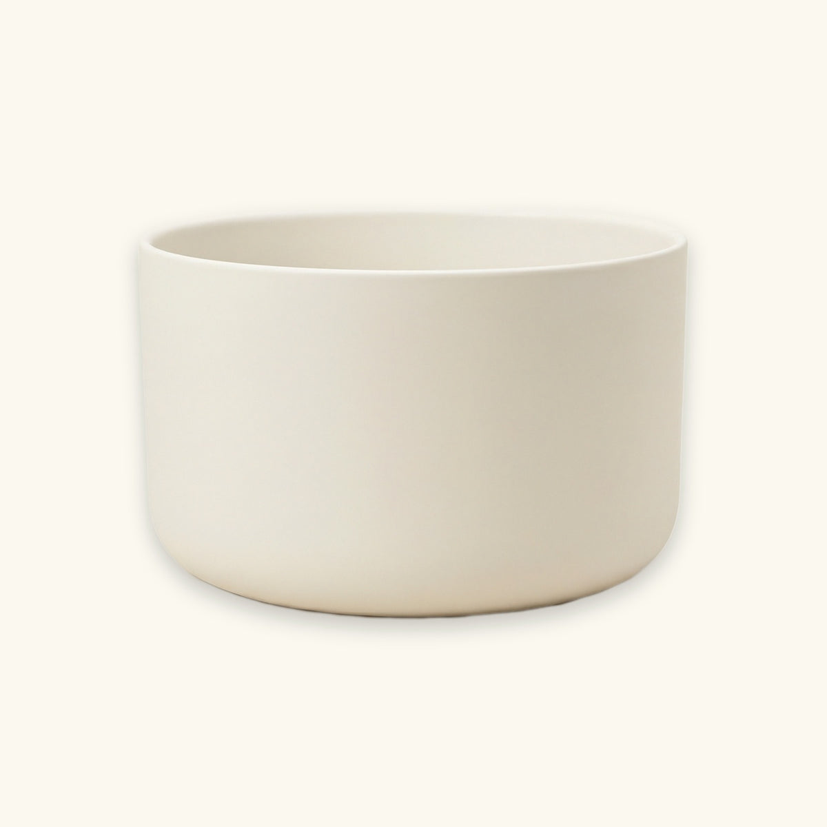 A minimalist, matte ceramic bowl in a warm off-white or cream color, photographed against a matching light cream background.