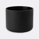 A matte black cylindrical planter or candle holder with a smooth, non-reflective finish, shown against a plain light gray background.