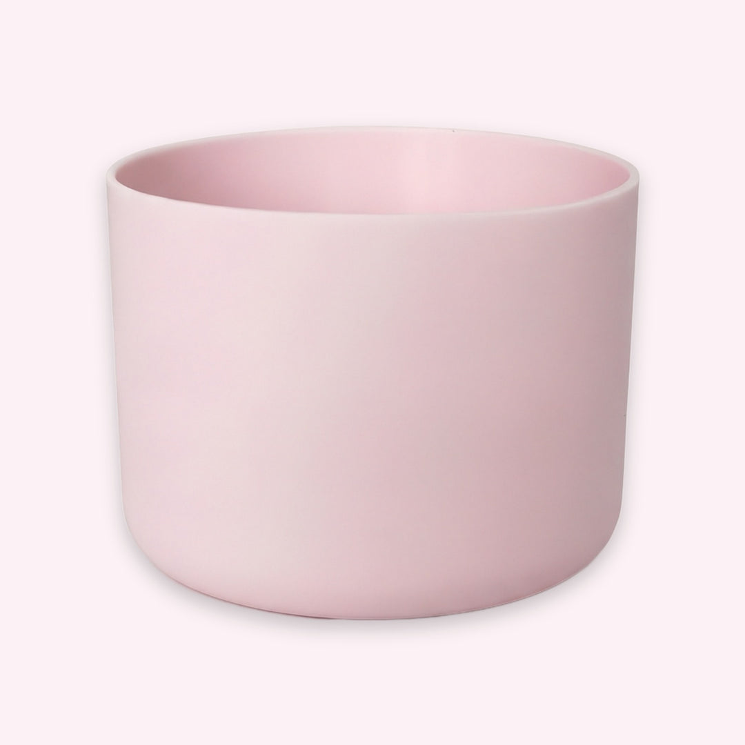 A minimalist, matte light pink cylindrical planter or candle holder, shown from a three-quarters angle on a clean, solid off-white background.