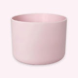 A minimalist, matte light pink cylindrical planter or candle holder, shown from a three-quarters angle on a clean, solid off-white background.