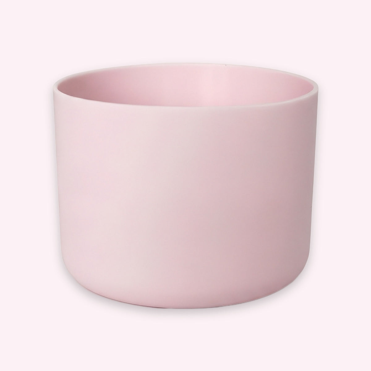 A minimalist, matte light pink cylindrical planter or candle holder, shown from a three-quarters angle on a clean, solid off-white background.