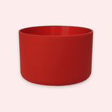 A matte red cylindrical planter or cup with a wide rim, shown against a solid pale pink background.