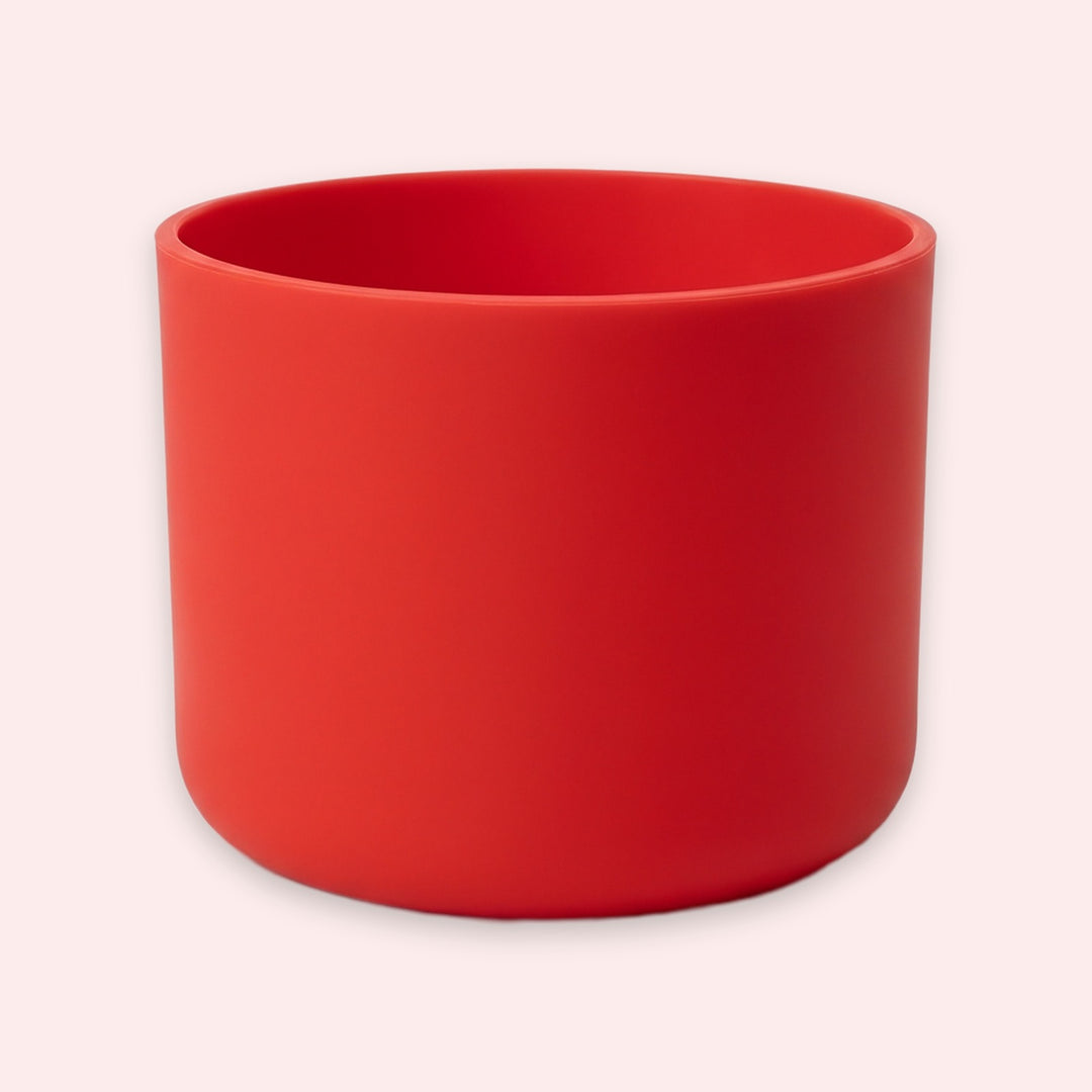 A matte red cylindrical planter pot with a wide rim, shown on a solid pale pink background.