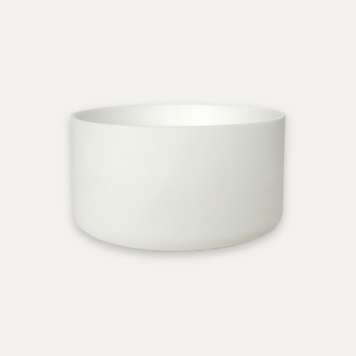 A minimalist white ceramic bowl with a matte finish, photographed from a direct side angle against a clean, off-white background.