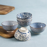 A set of five ceramic bowls with blue and white Japanese patterns, including one bowl shown upside down, arranged on a light blue surface with wooden boards as props.
