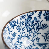 Close-up of a white ceramic bowl featuring a classic blue floral and leaf pattern, with a thin brown rim.