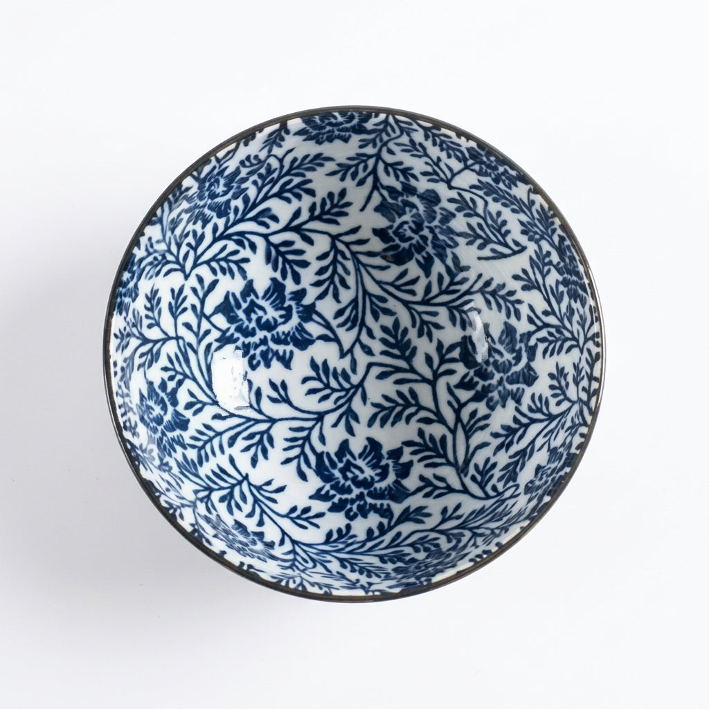 A round ceramic bowl with a blue floral and botanical pattern on a white background, photographed from directly above against a light gray backdrop.