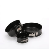 Three black non-stick springform cake pans of different sizes with silver metal clamps, arranged on a clean white background.