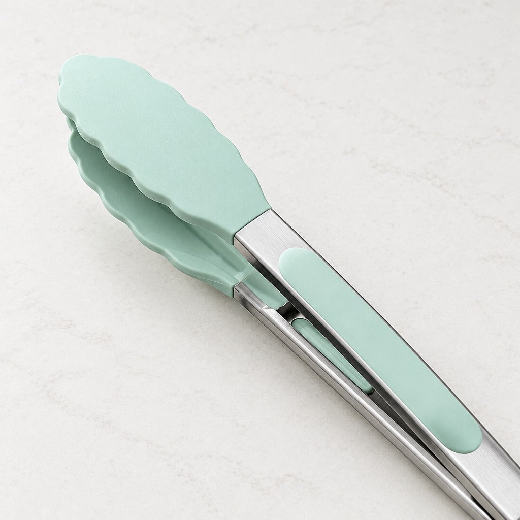 Mint green silicone-tipped metal kitchen tongs with a brushed stainless steel clip, shown on a light marble surface.