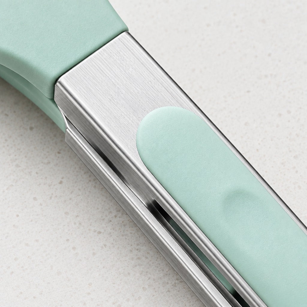 Close-up of a kitchen utensil with a brushed silver metal body and mint green silicone accents, resting on a light speckled countertop.
