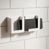 A pair of white wall-mounted phone holders with a smartphone inserted into the right holder, mounted on a white tiled wall.