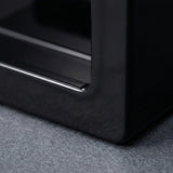 Close-up of a glossy black furniture piece, showing a corner with a metallic trim edge resting on a textured gray carpet.