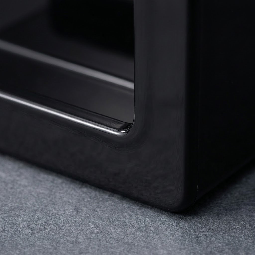 Close-up of a glossy black furniture piece, showing a corner with a metallic trim edge resting on a textured gray carpet.