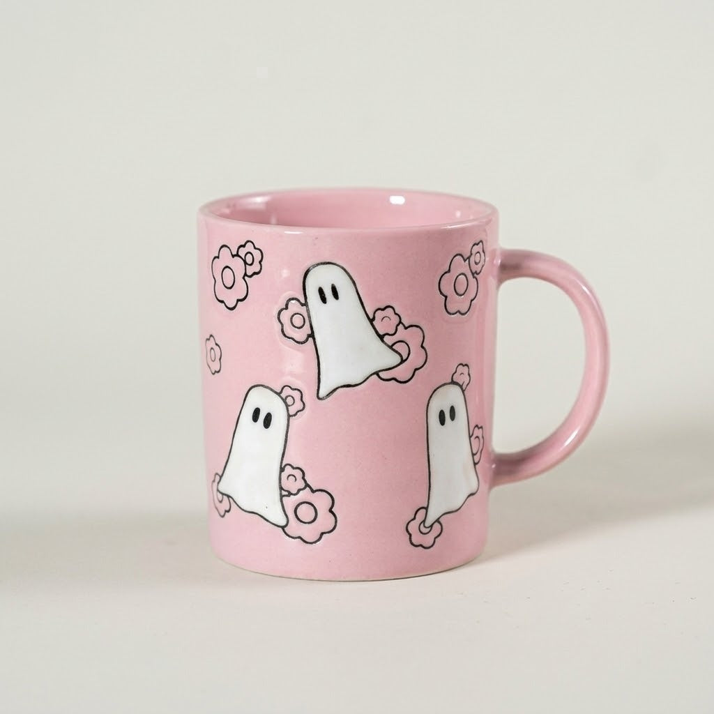 A pink ceramic mug decorated with three cartoon ghosts and small flowers, set against a plain light gray background.