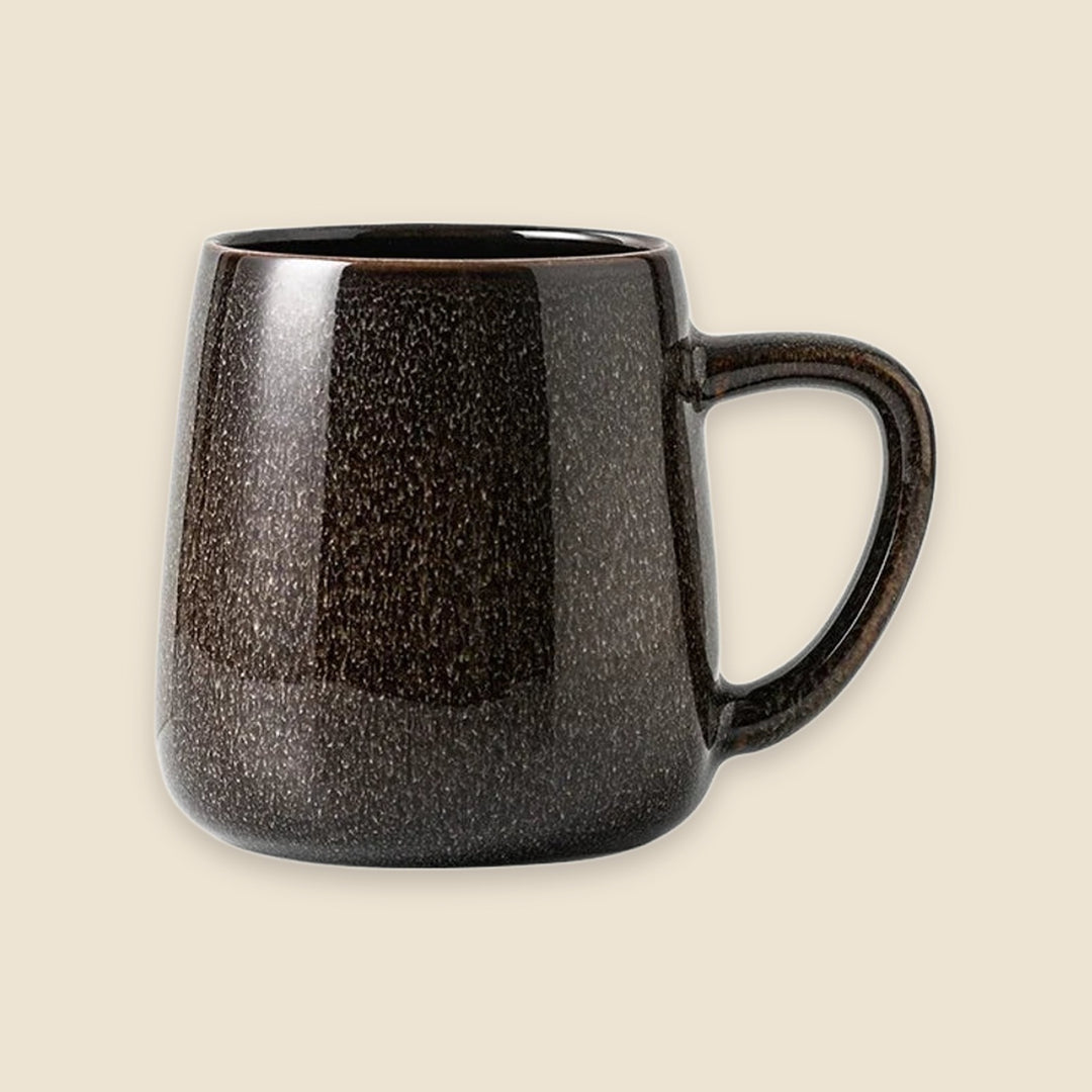 A dark brown ceramic mug with a speckled, textured glaze and a C-shaped handle, shown against a solid light beige background.