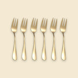 Six gold-colored metal forks arranged in a row on a light beige background.