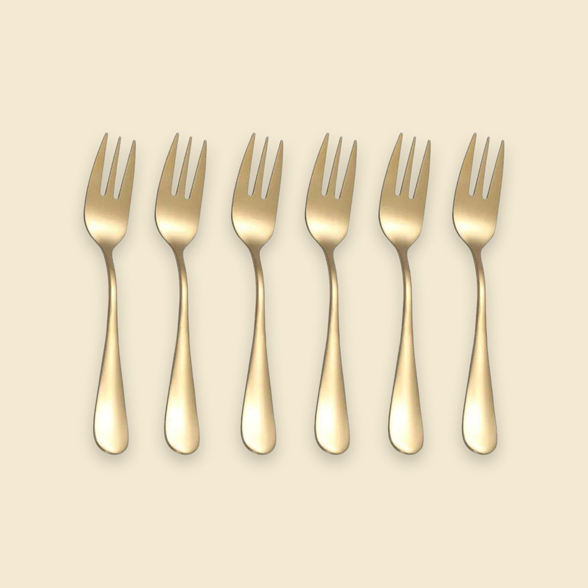 Six gold-colored metal forks arranged in a row on a light beige background.