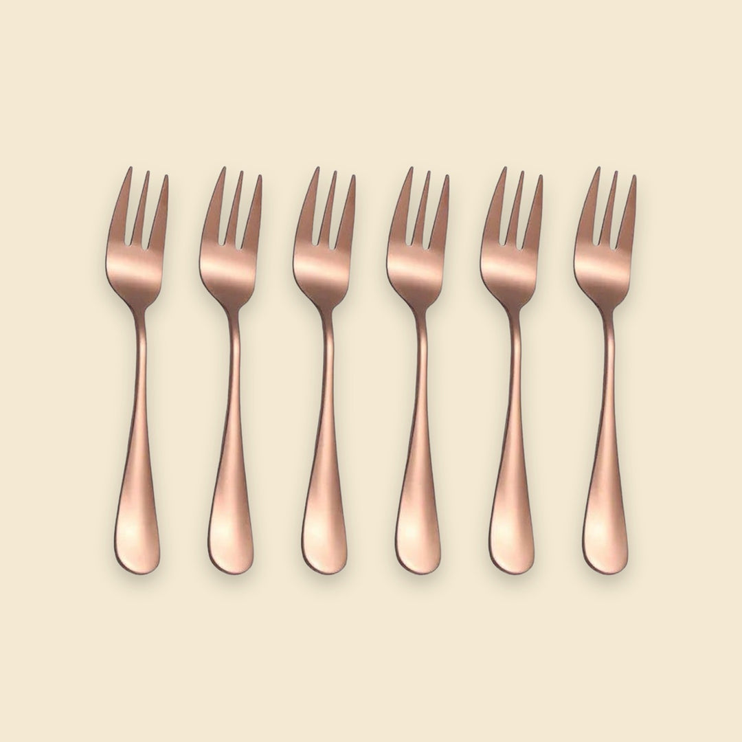 Six rose gold metal forks arranged in a neat horizontal row on a solid light beige background.