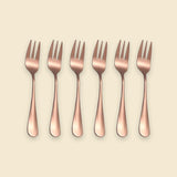 Six rose gold metal forks arranged in a neat horizontal row on a solid light beige background.