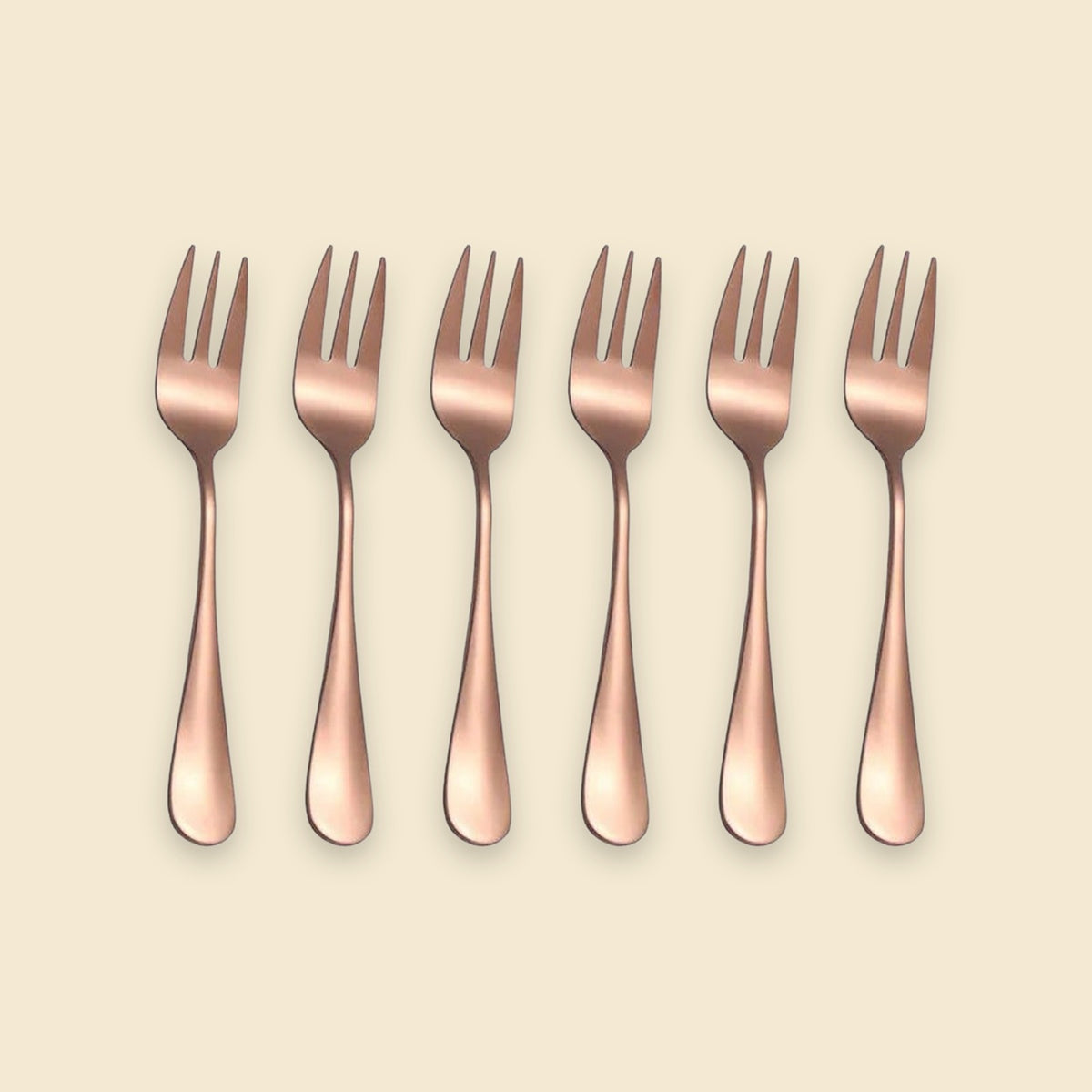 Six rose gold metal forks arranged in a neat horizontal row on a solid light beige background.