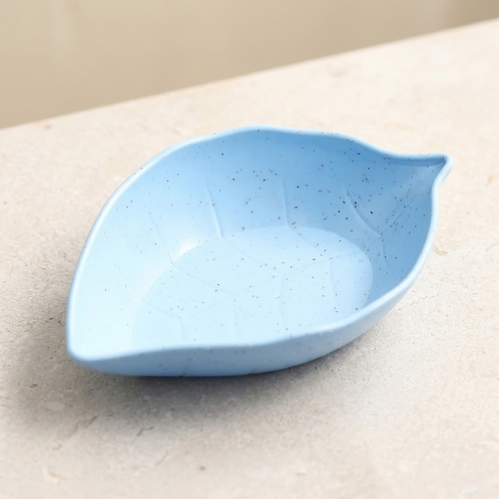 A light blue ceramic leaf-shaped dish with subtle dark speckles, resting on a light beige stone surface.