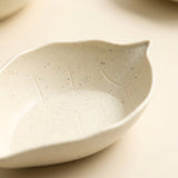 Close-up of a speckled cream leaf-shaped dish with raised vein details on a pale beige surface.