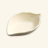 A leaf-shaped ceramic dish with a speckled cream finish, photographed on a solid off-white background.