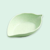 A light green ceramic leaf-shaped bowl with subtle dark speckles, shown on a solid pale mint green background.