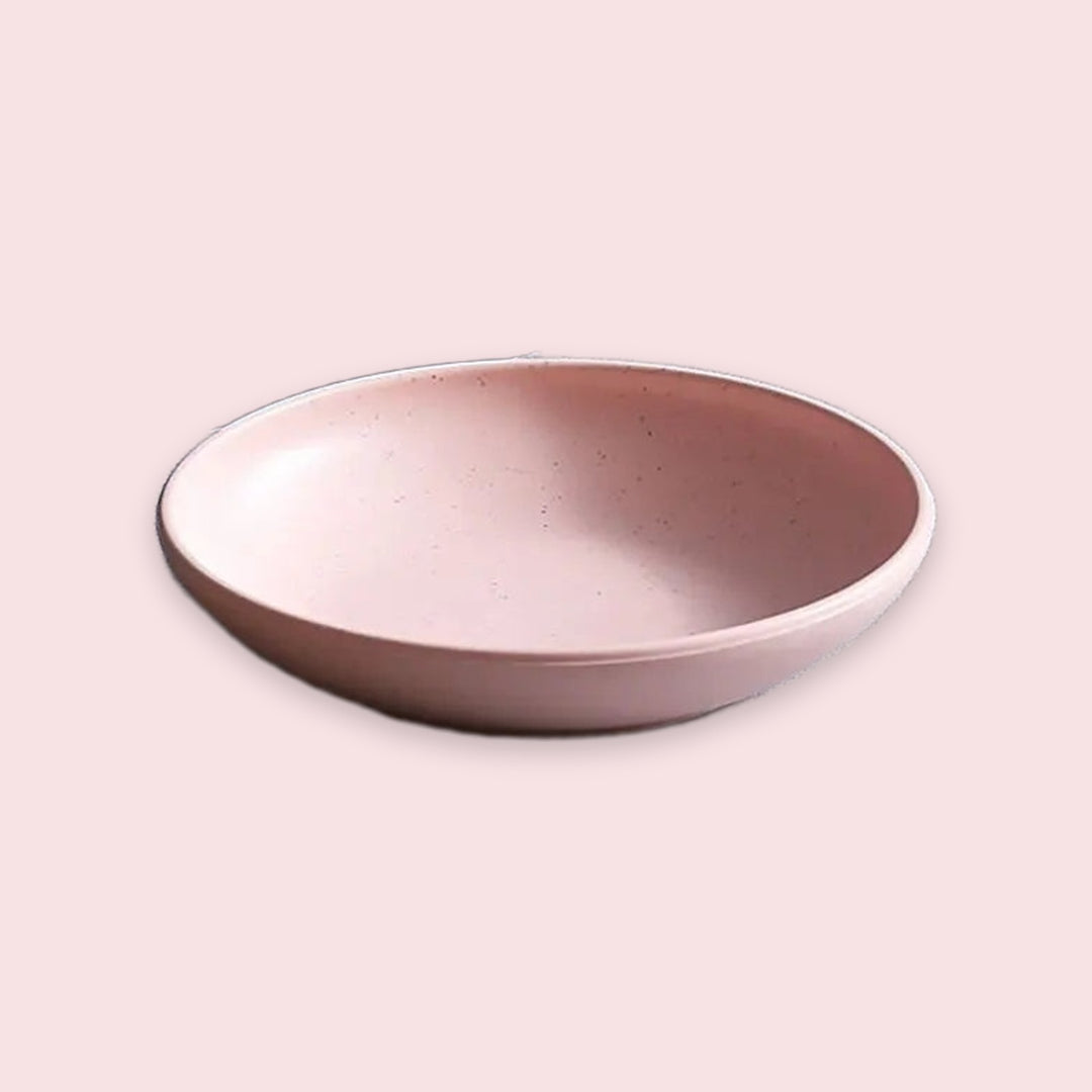 A shallow round ceramic bowl with a speckled off-white glaze and a slightly darker rim, shown on a plain light beige background.