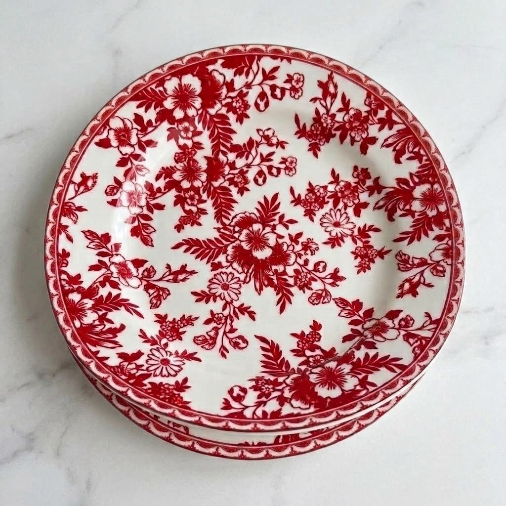 Stacked white plates with red floral patterns and decorative borders rest on a pale marble surface.