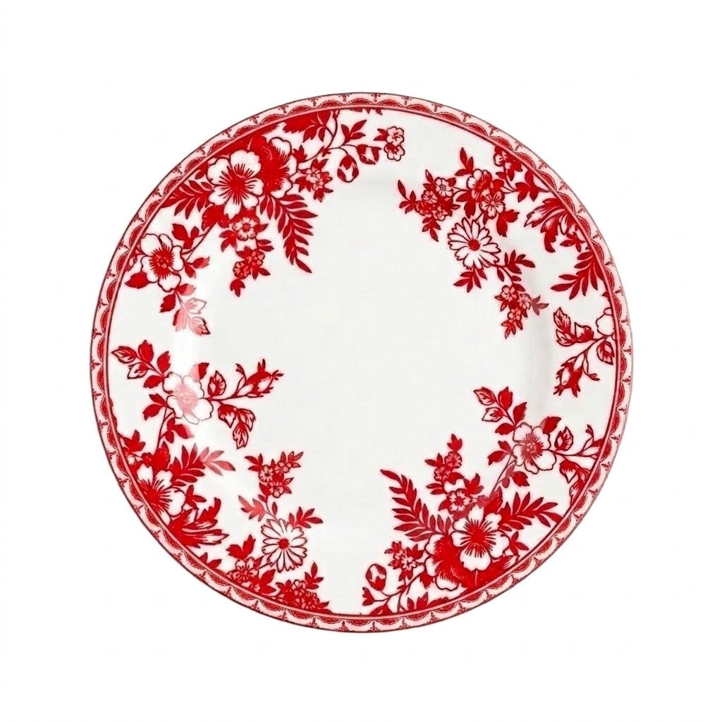 A round white plate with red flowers and leaves around its border sits against a white background.
