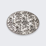 A white plate covered in black floral patterns with a matching decorative rim sits against a light grey background.