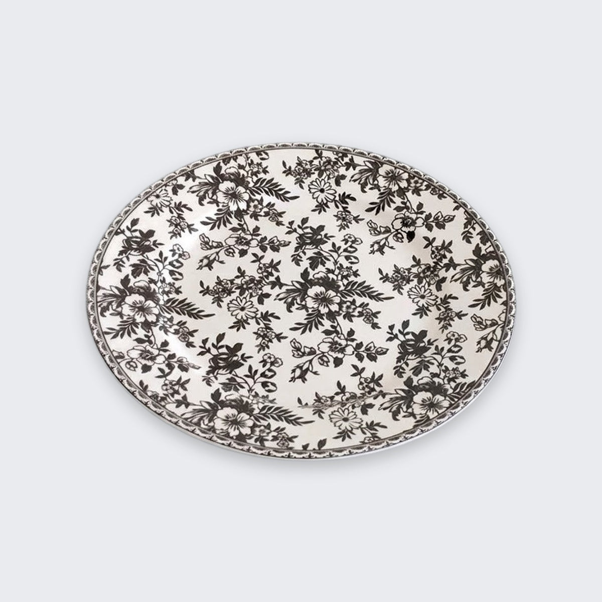 A white plate covered in black floral patterns with a matching decorative rim sits against a light grey background.