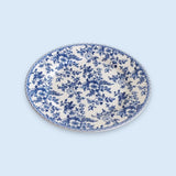 A white plate covered in blue floral patterns with a matching decorative rim sits against a pale blue background.